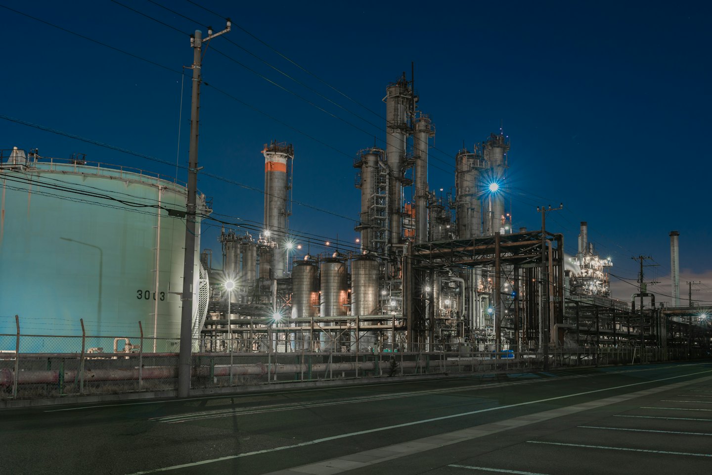 Brightly lit industrial refinery with pipes and towers at night.